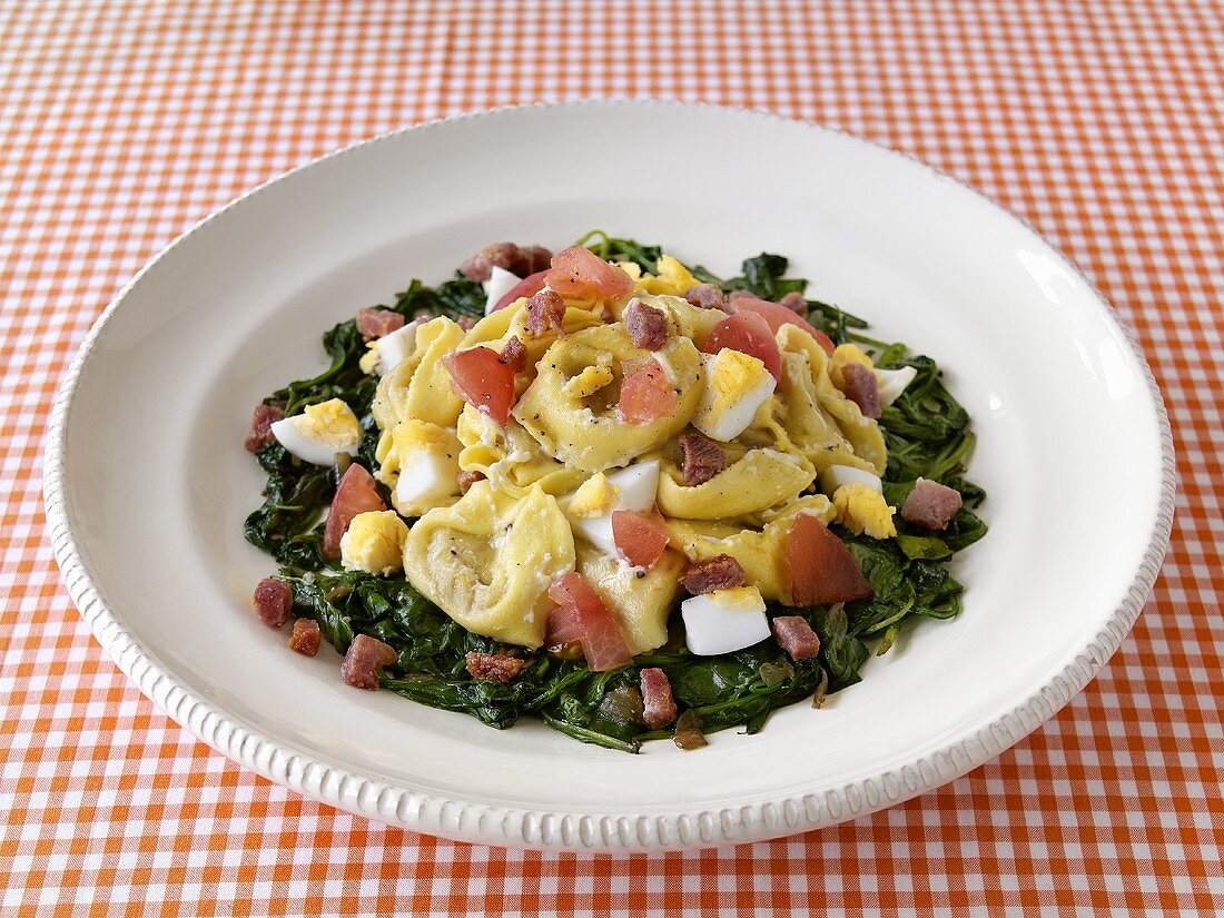 Tortellini mit gekochten Eiern und Speckwürfeln auf Spinat