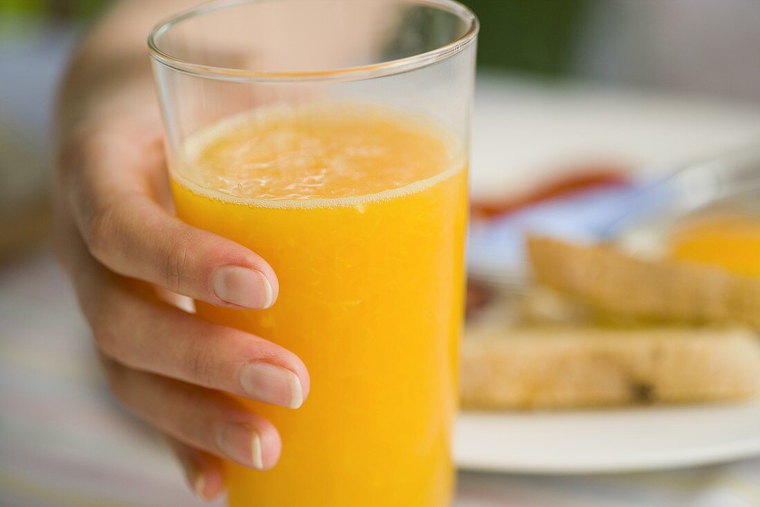 Hand hält ein Glas Orangensaft