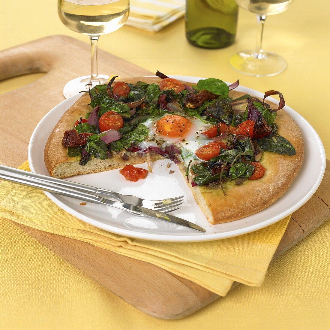 Pizza topped with fried egg, spinach, cherry tomatoes and onions