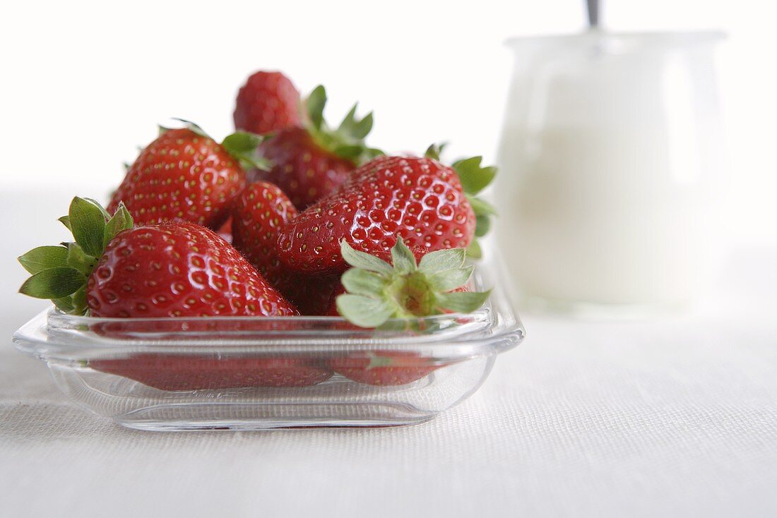 Fresh strawberries in glass dish, jar of yoghurt behind