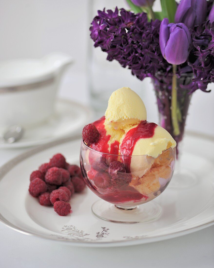 Vanilleeis mit Himbeersauce, im Hintergrund Frühlingsblumen