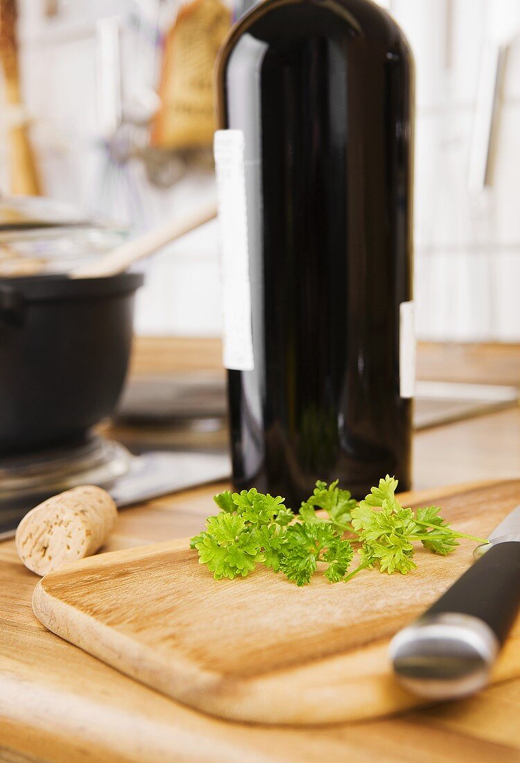 Parsley on wooden board with knife, bottle of red wine behind
