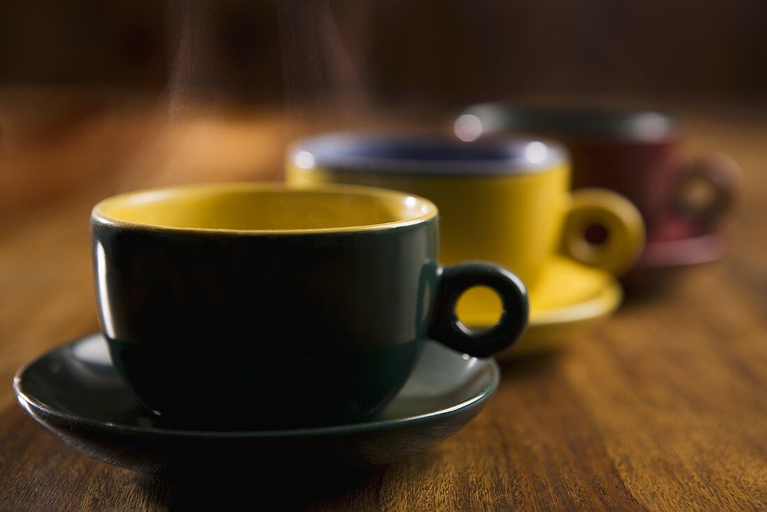 Steaming tea or coffee in three coloured cups and saucers