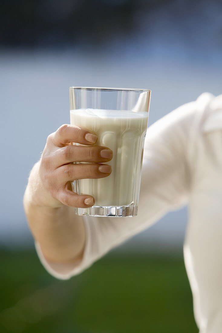 Hand hält ein Glas Milch