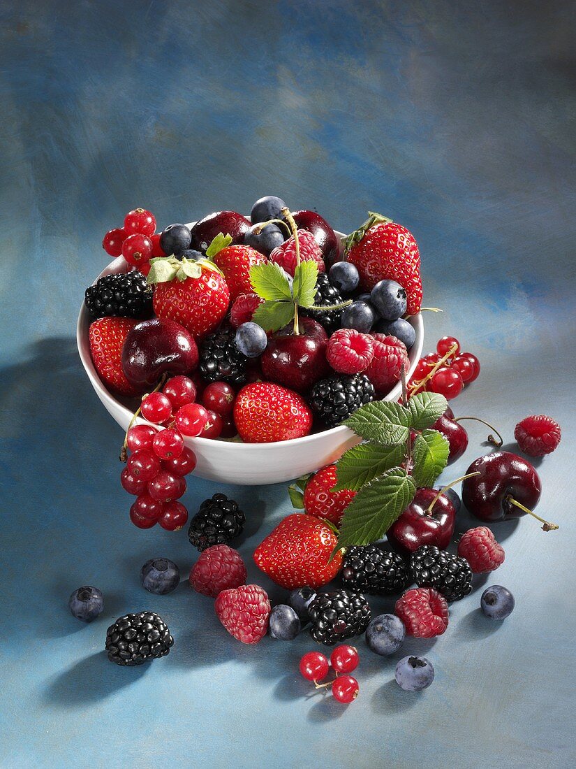 Mixed berries and cherries in and in front of bowl