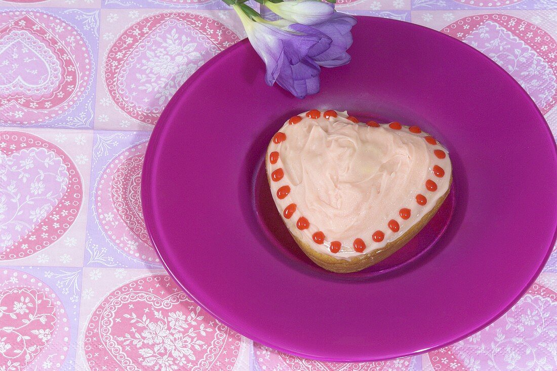 A heart-shaped cake with pink cream and red spots