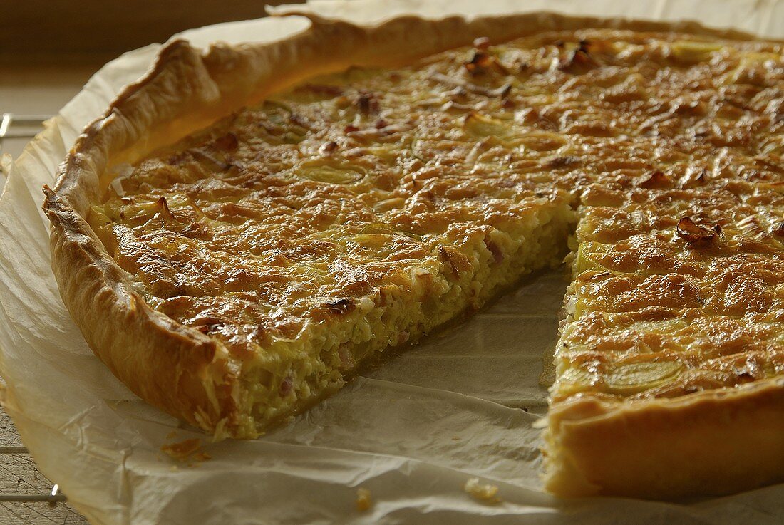 An onion quiche with a piece removed on baking parchment