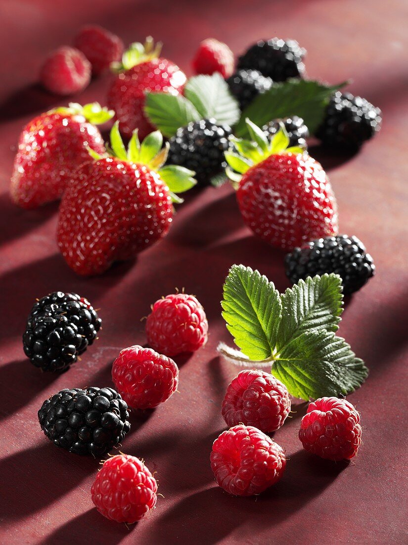 Strawberries, blackberries and raspberries on red background