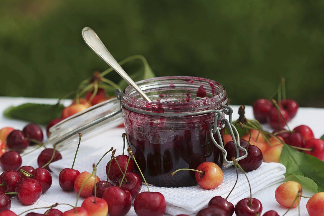 A jar of cherry jam with spoon and cherries