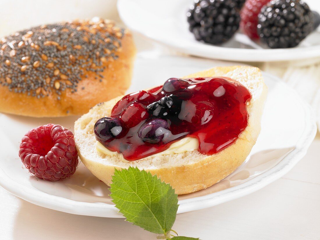 A bread roll spread with butter and berry jam