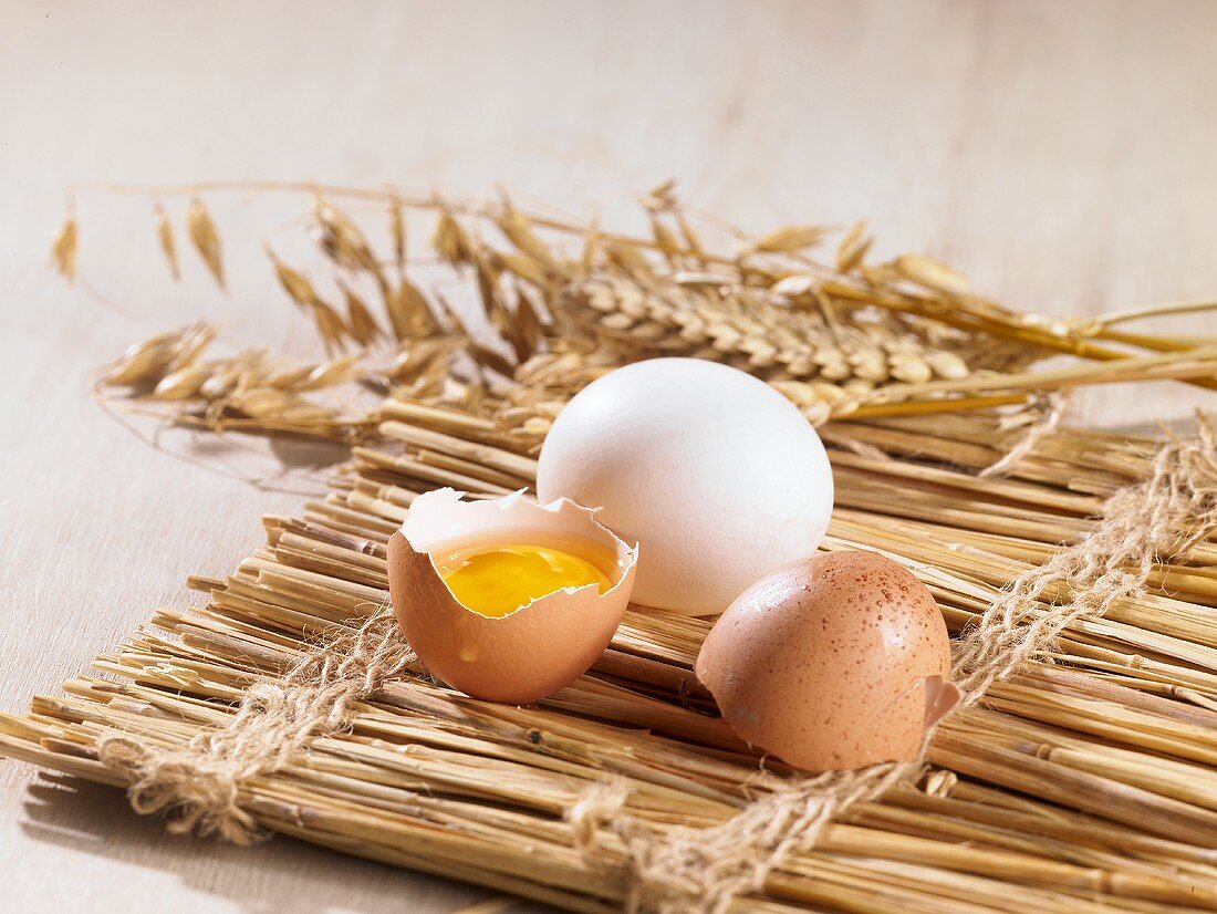 A cracked open egg and ears of wheat on a straw mat