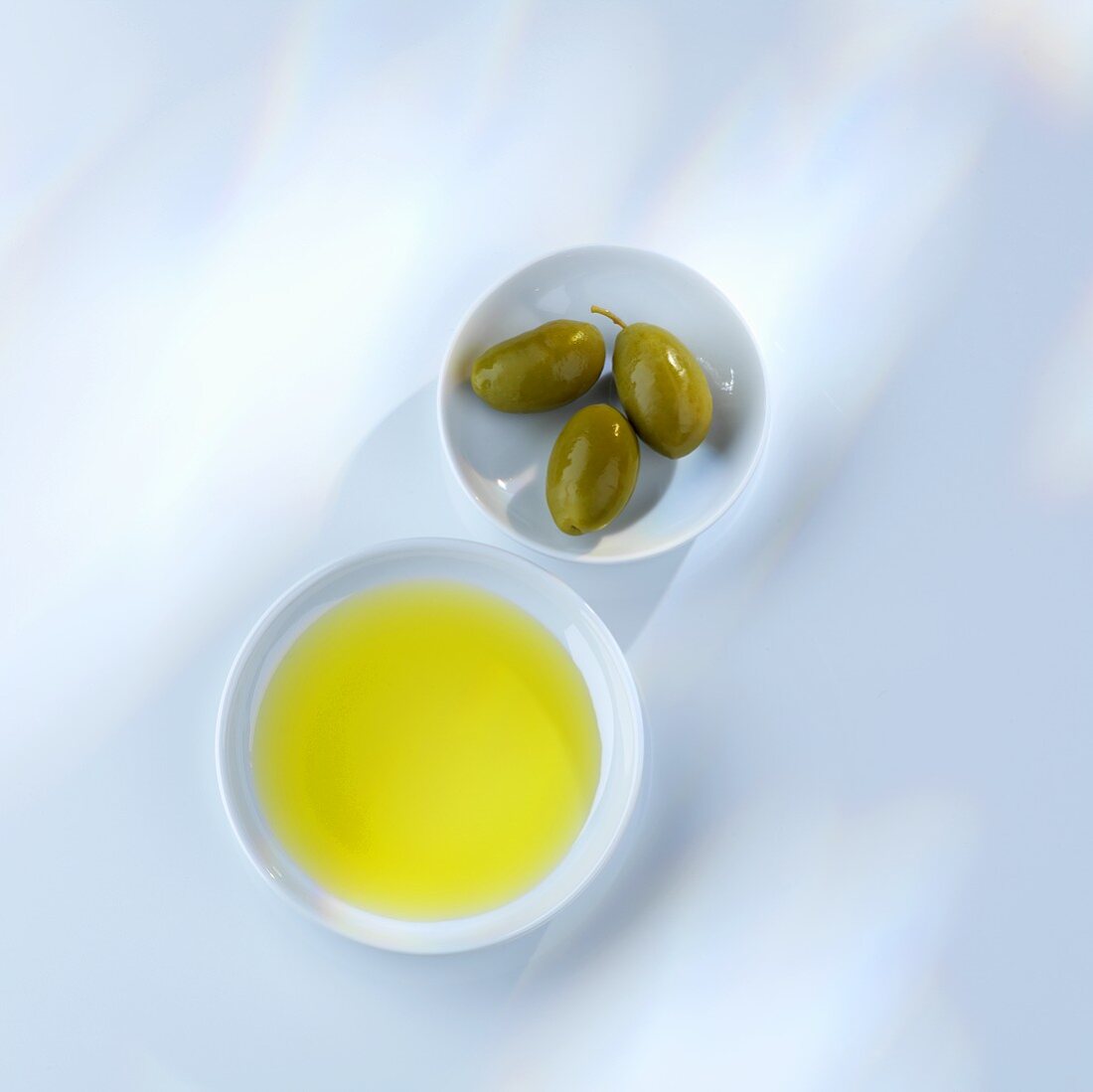 Olivenöl und grüne Oliven in Schälchen (Draufsicht)