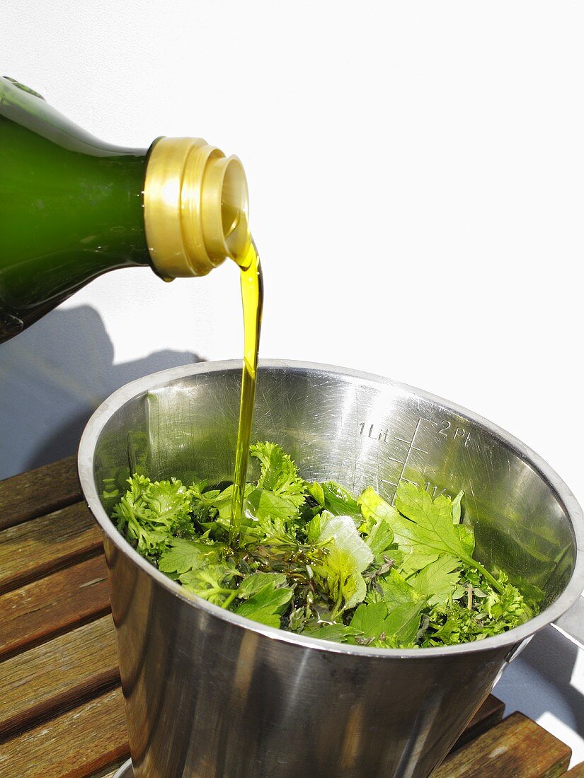 Pouring olive oil over herbs (ingredients for pesto)