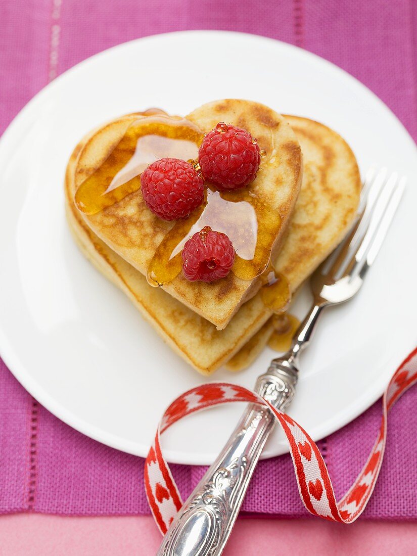 Heart-shaped pancakes with raspberries and maple syrup