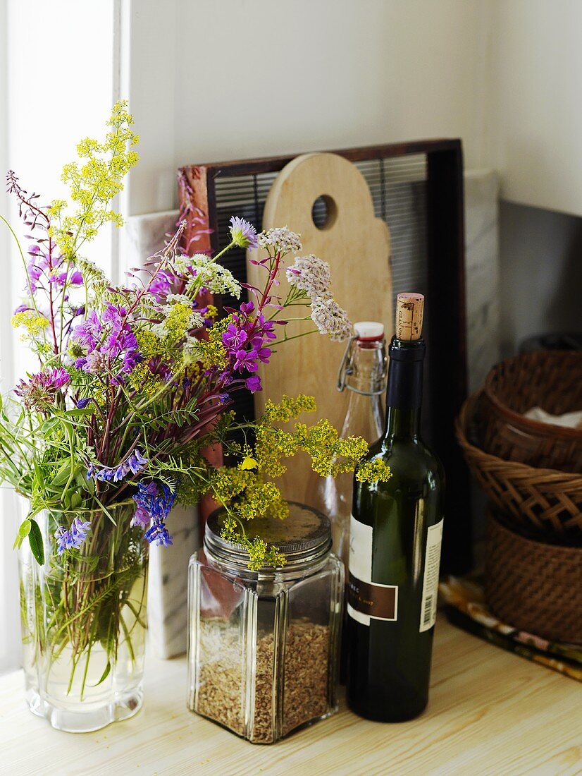 Vase mit Blumen, Rotweinflasche und Küchenutensilien