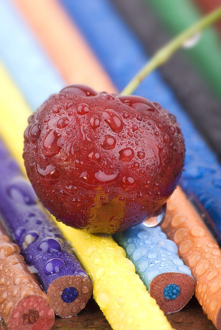 A cherry with drops of water on crayons