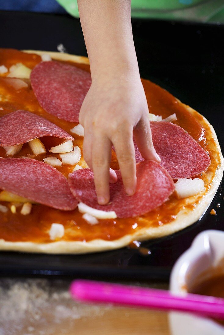 Kinderhand belegt Pizza mit Salamischeiben