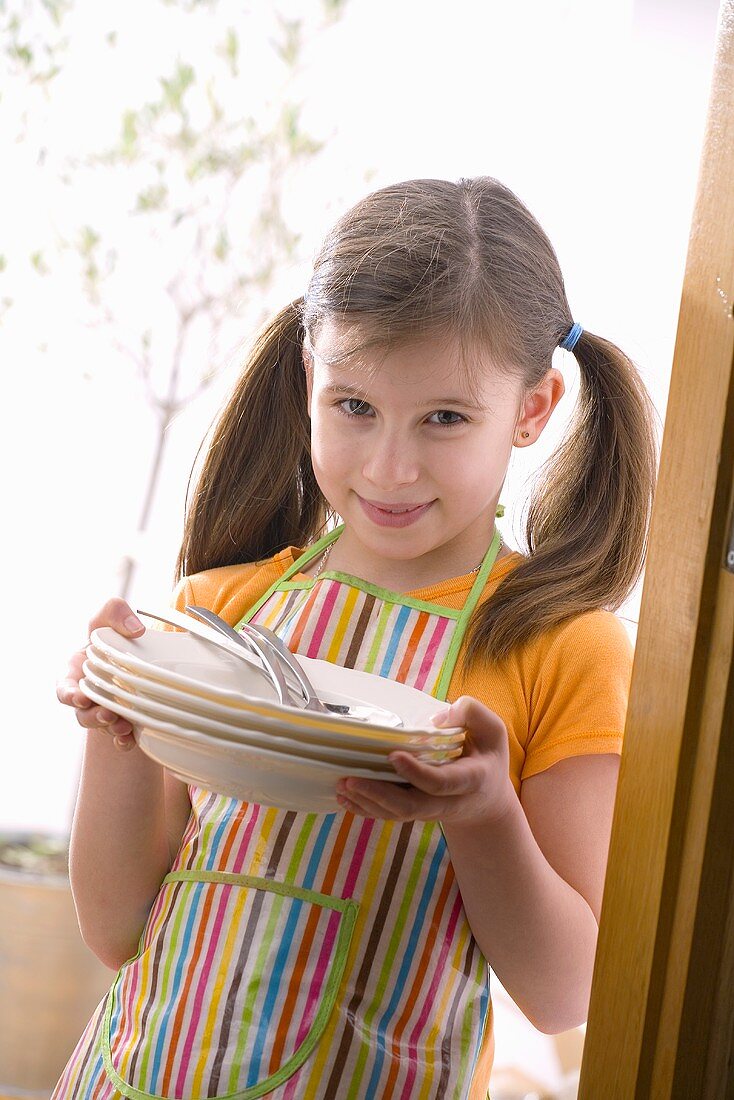 Mädchen mit Schürze hält Teller und Besteck