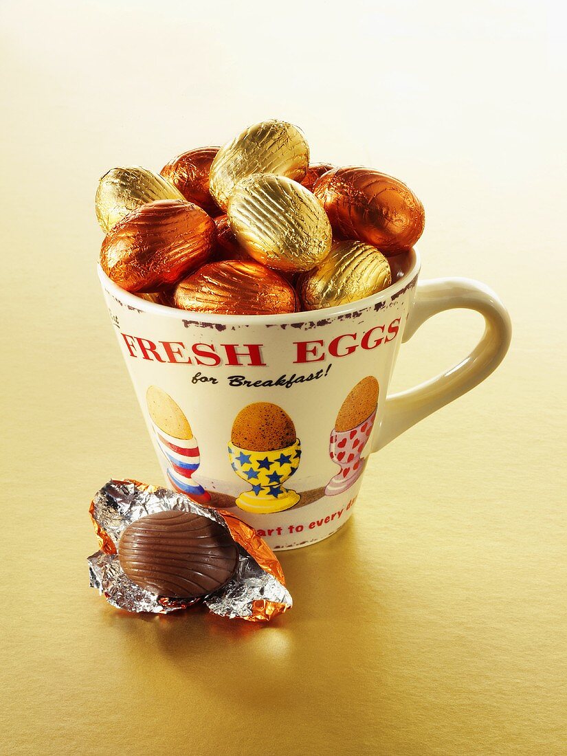Foil-wrapped chocolate eggs in and beside a cup