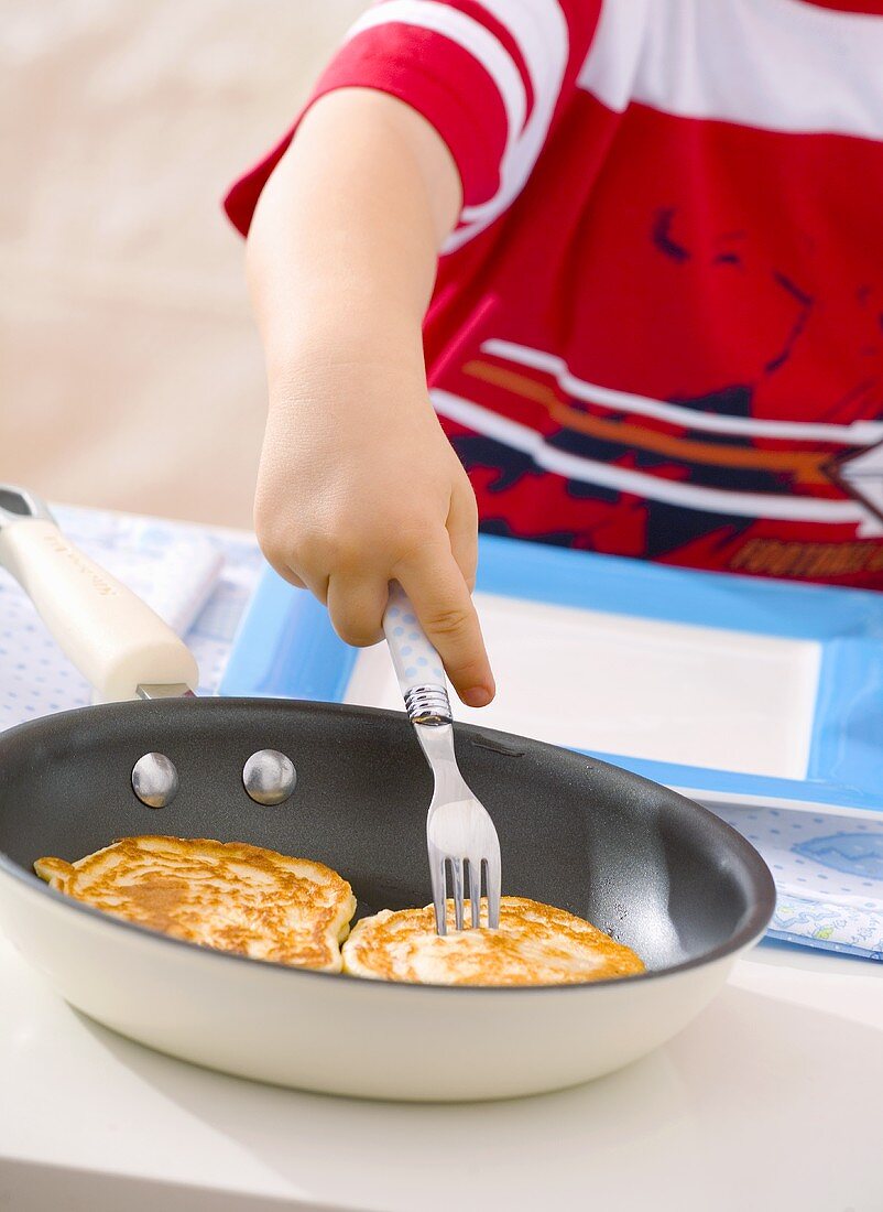 Kleiner Junge nimmt Pancake aus der Pfanne