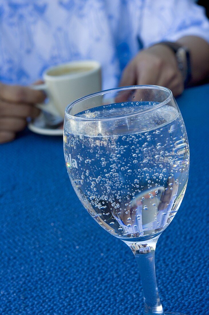 A glass of water, man with a cup of espresso in background
