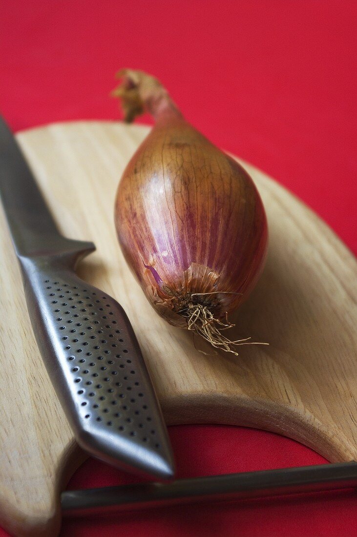 A shallot with a knife on a chopping board