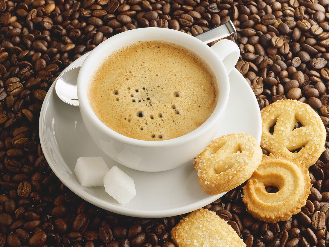 Eine Tasse Kaffee mit Zuckerwürfeln und Gebäck
