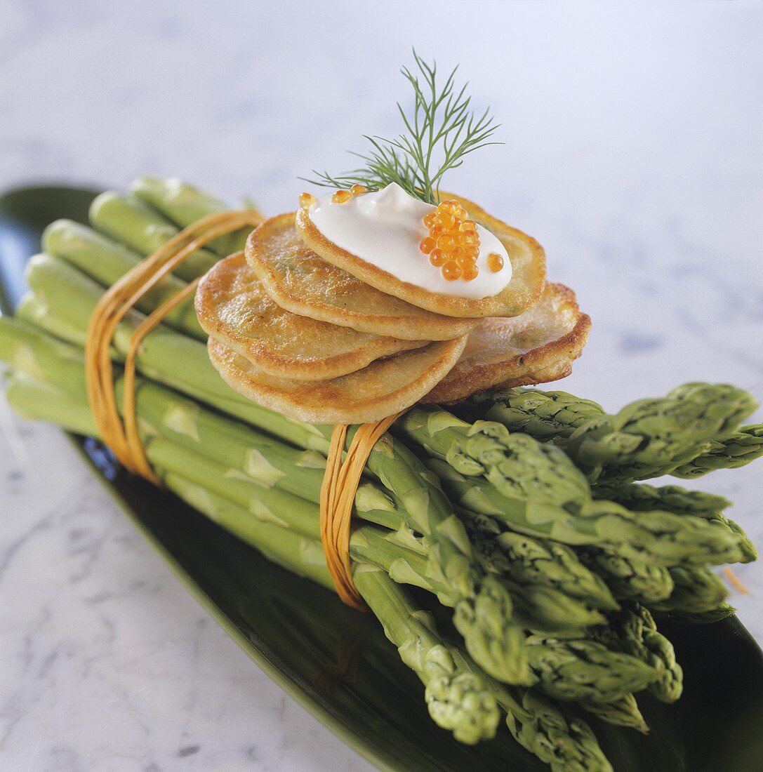 Blinis with sour cream and caviar on green asparagus