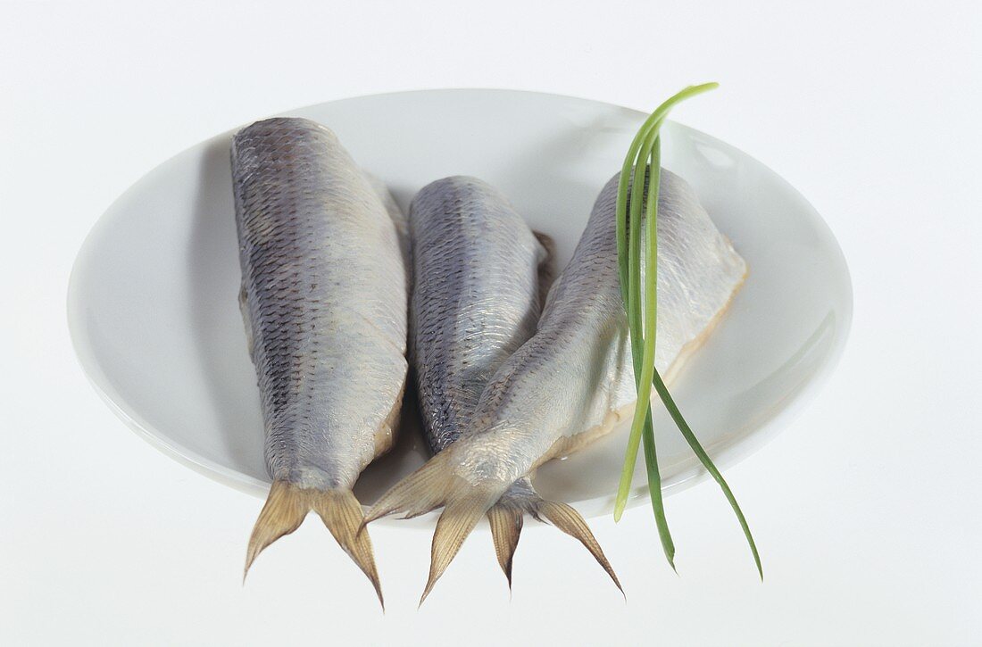 Three herrings without heads on white plate