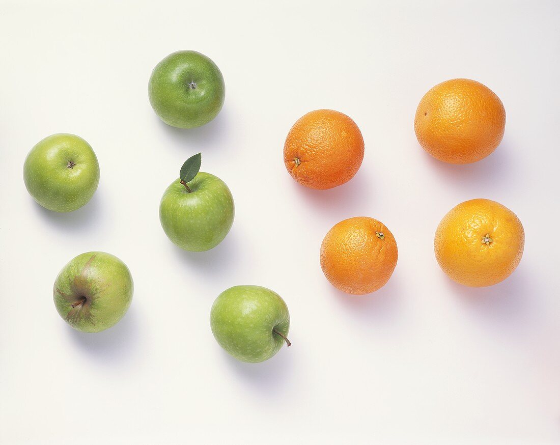 Five green apples & four oranges against a white background