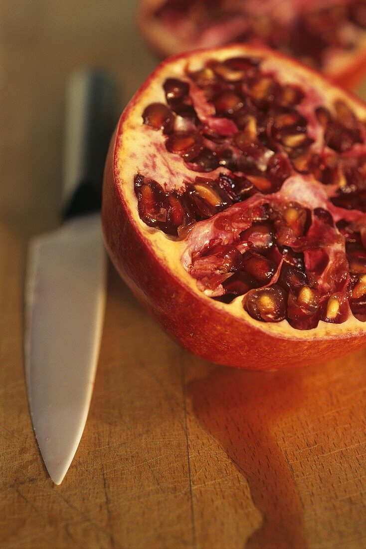 Halved pomegranate on wooden board with knife