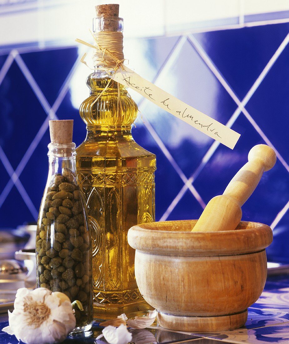 Garlic, bottle of capers, bottle of almond oil & wooden mortar & pestle