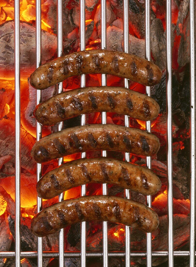 Five sausages on barbecue rack over burning charcoal