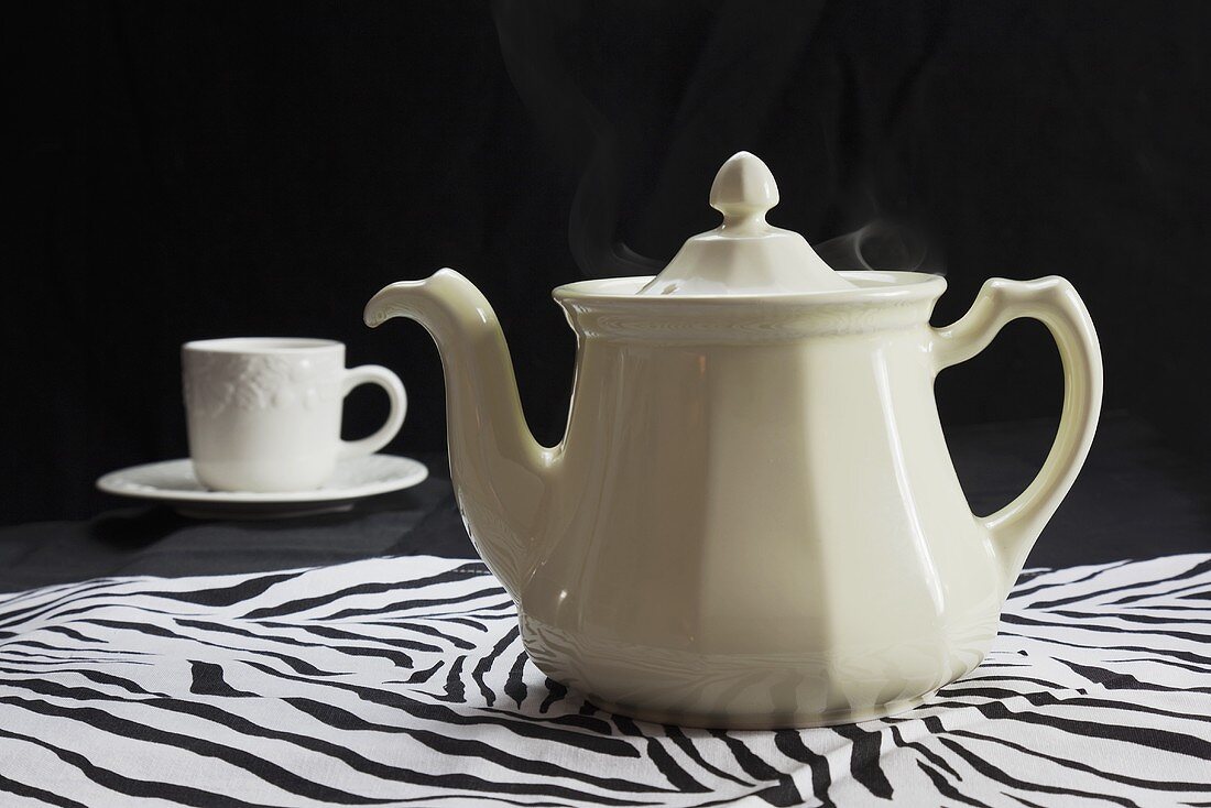 Teekanne und Teetasse auf Tischtuch mit Zebramuster