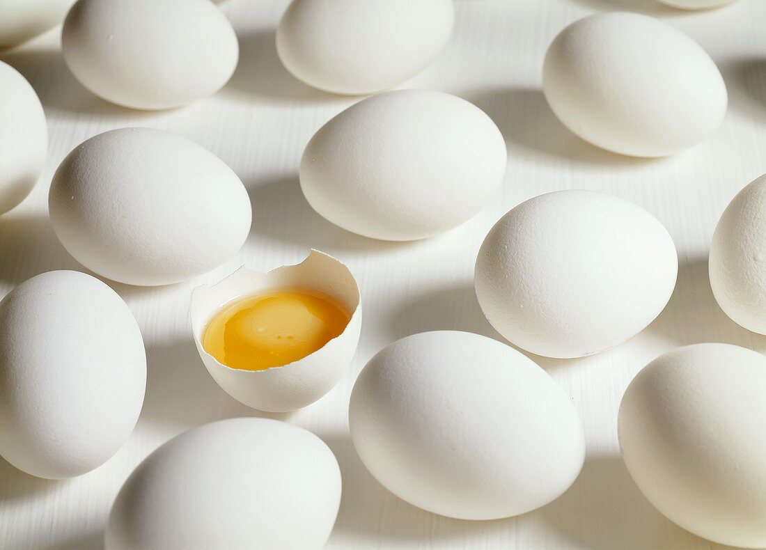 Viele rohe weiße Eier, eines davon aufgeschlagen
