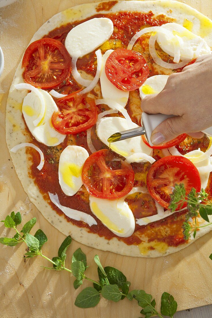 Pizza mit Olivenöl beträufeln