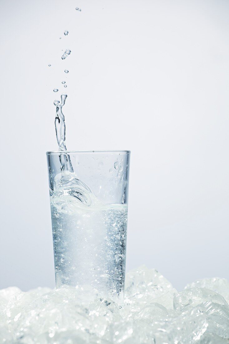 Ice cube falling into glass of ouzo