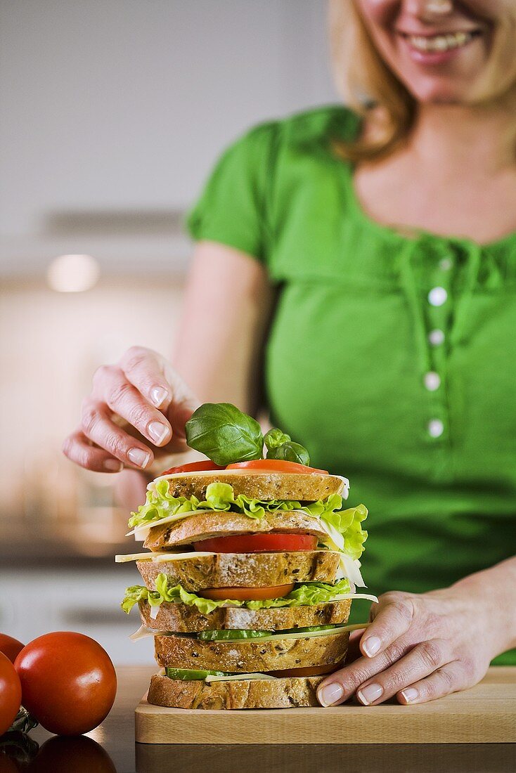 Woman garnishing a multilayer sandwich with basil