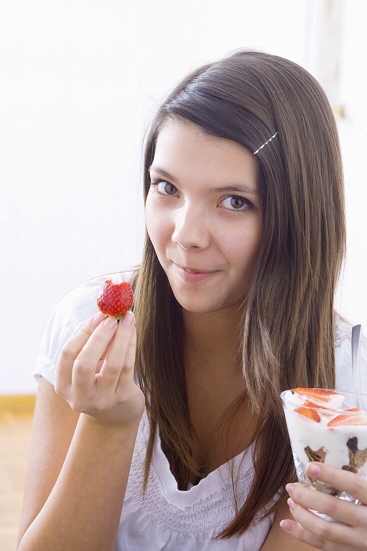 Mädchen hält Joghurtmüsli und angebissene Erdbeere