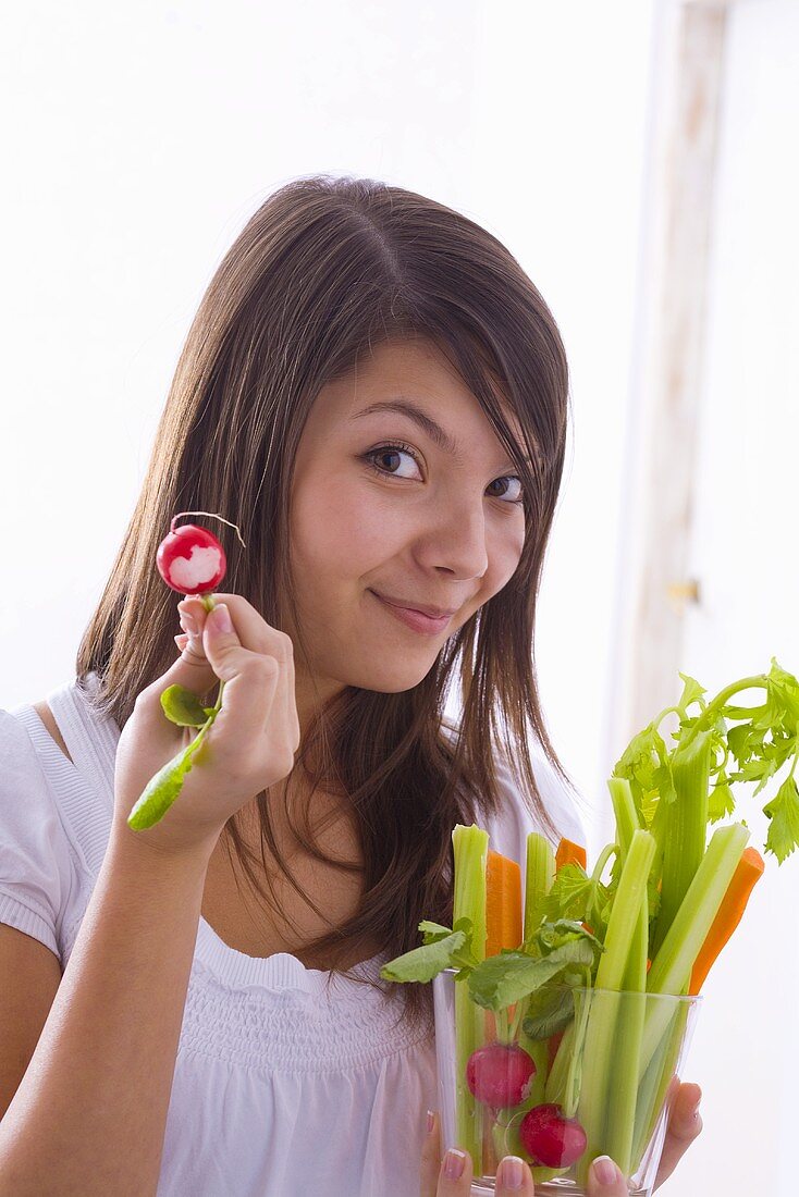 Mädchen hält rohes Gemüse und angebissenes Radieschen