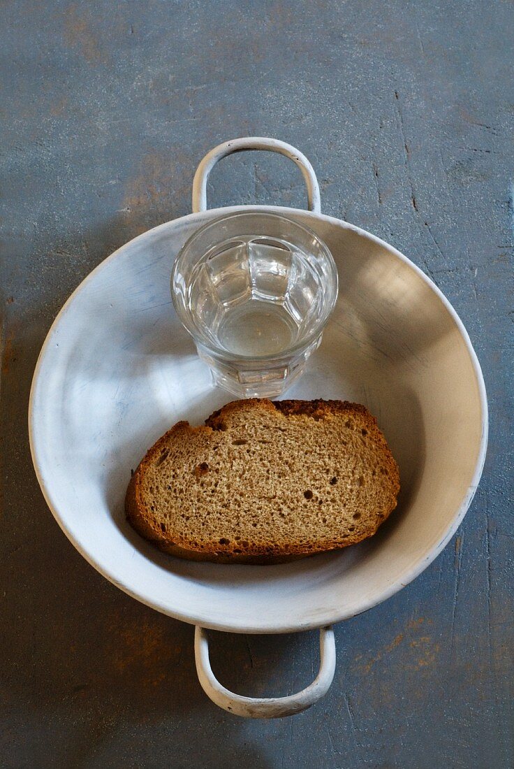 Bread and water in a dish on a grey background