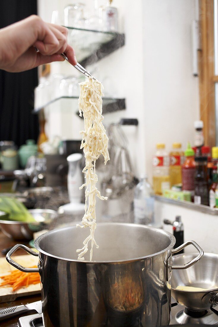 Putting Asian noodles in a saucepan with boiling water