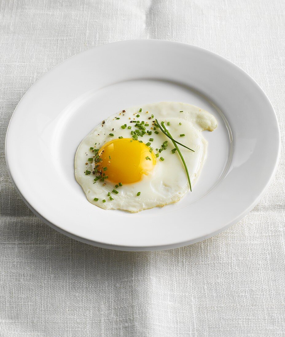 Plate with fried egg and chives on a linen tablecloth