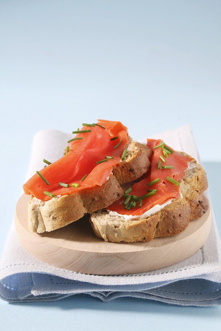 Two slices of bread with smoked salmon and chives on a wooden plate