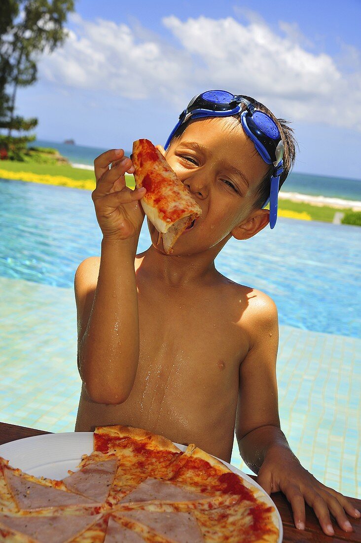 Boy with swimming goggles on head eating pizza on beach