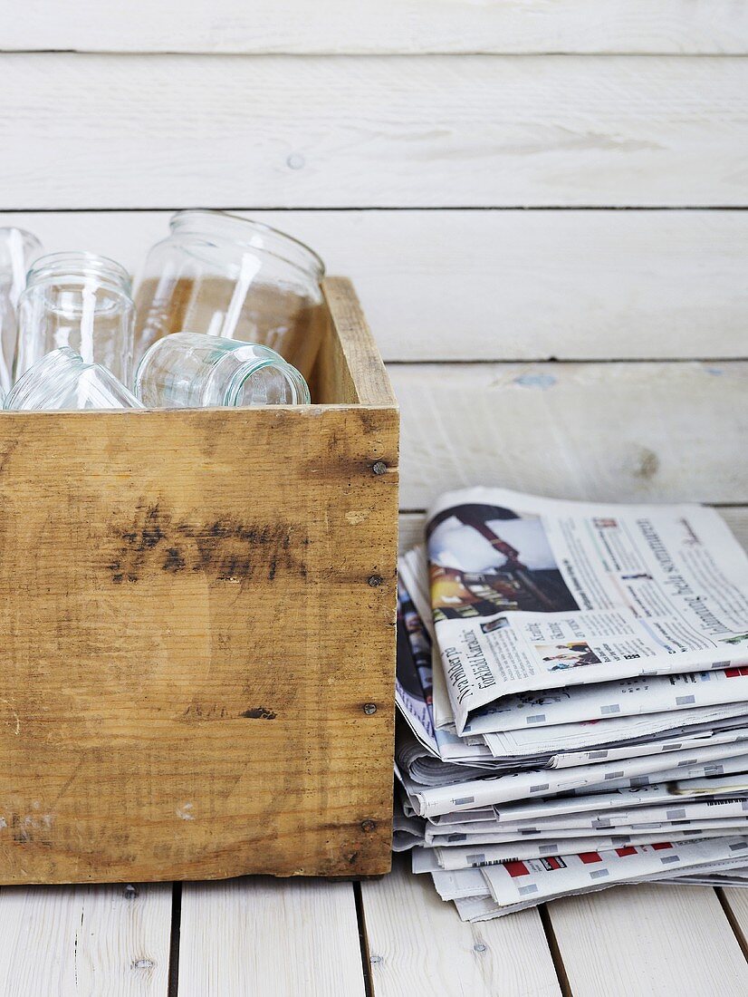 Empty glasses in wooden box beside pile of newspapers