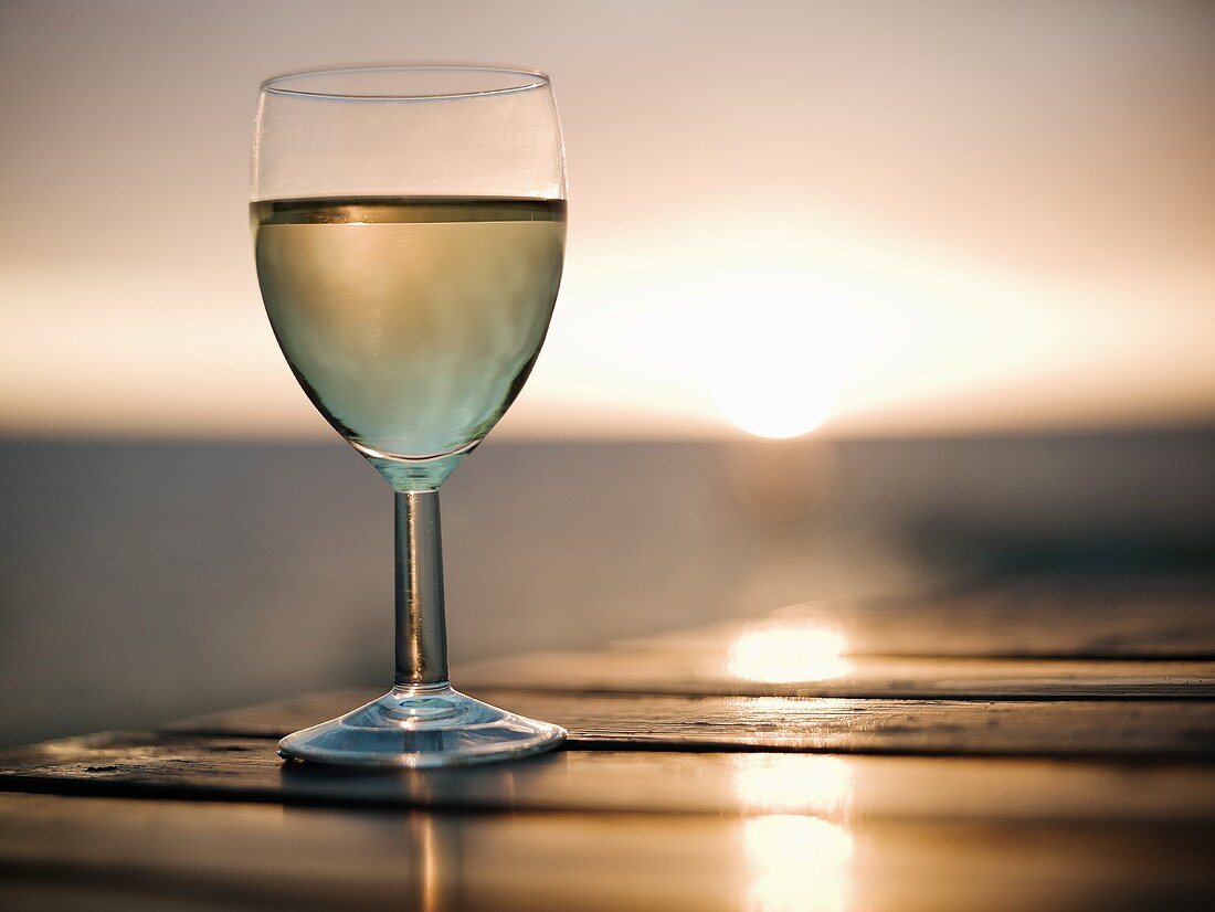 Weissweinglas auf Tisch vor untergehender Sonne