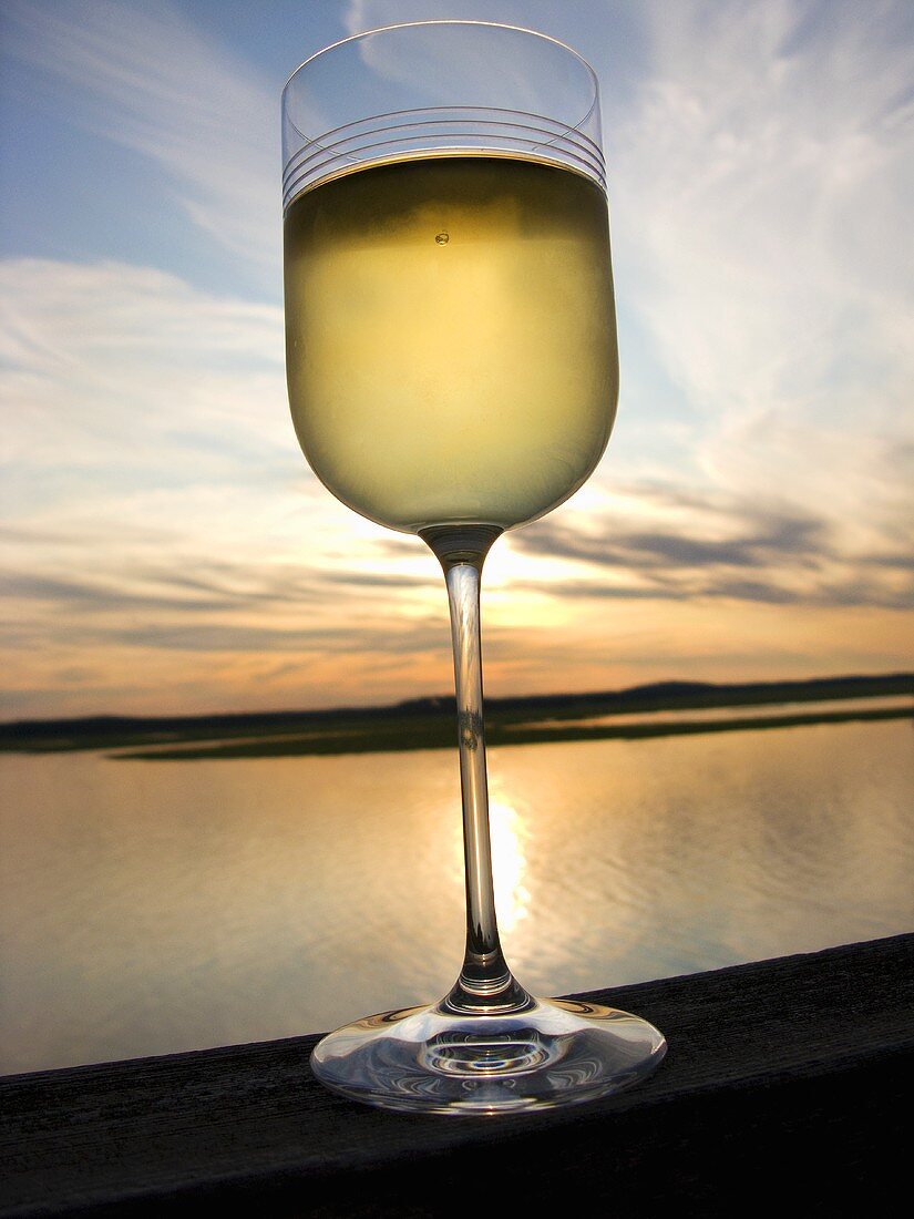 Weissweinglas vor Sonnenuntergang am Meer