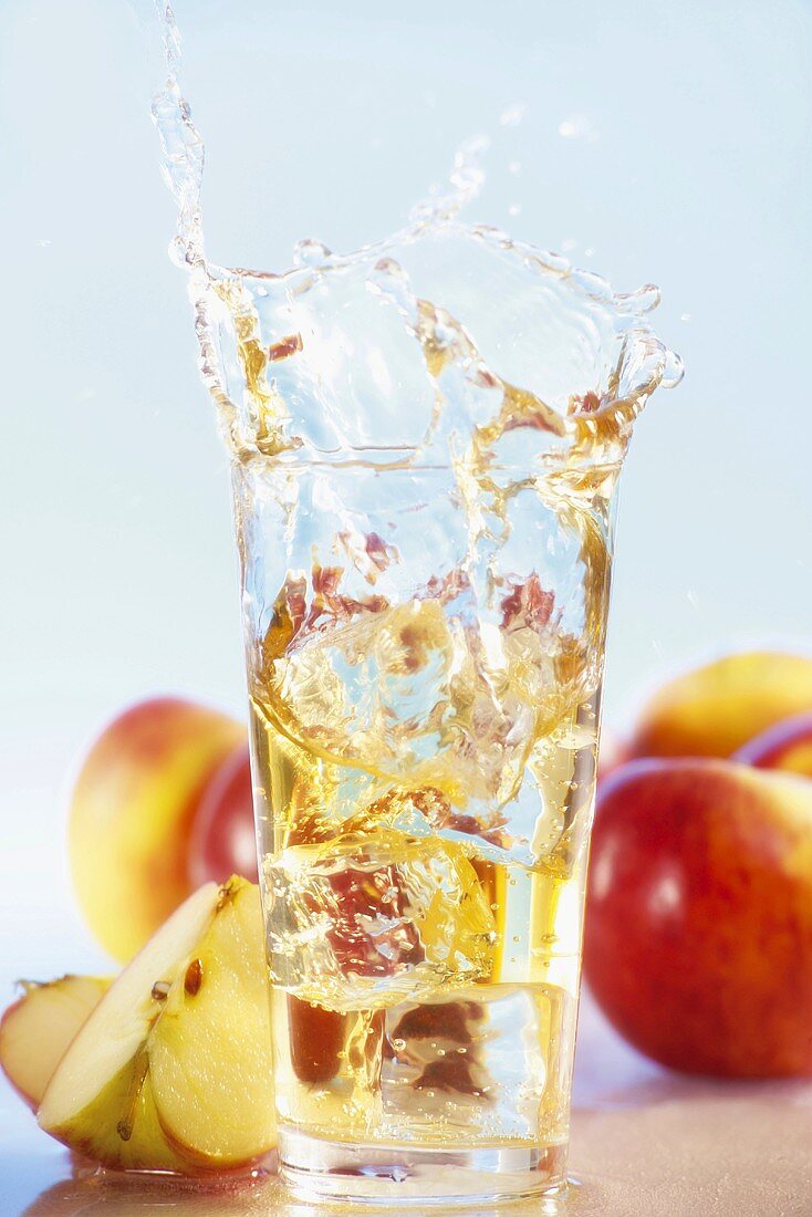 Ice cube falling into glass of apple juice