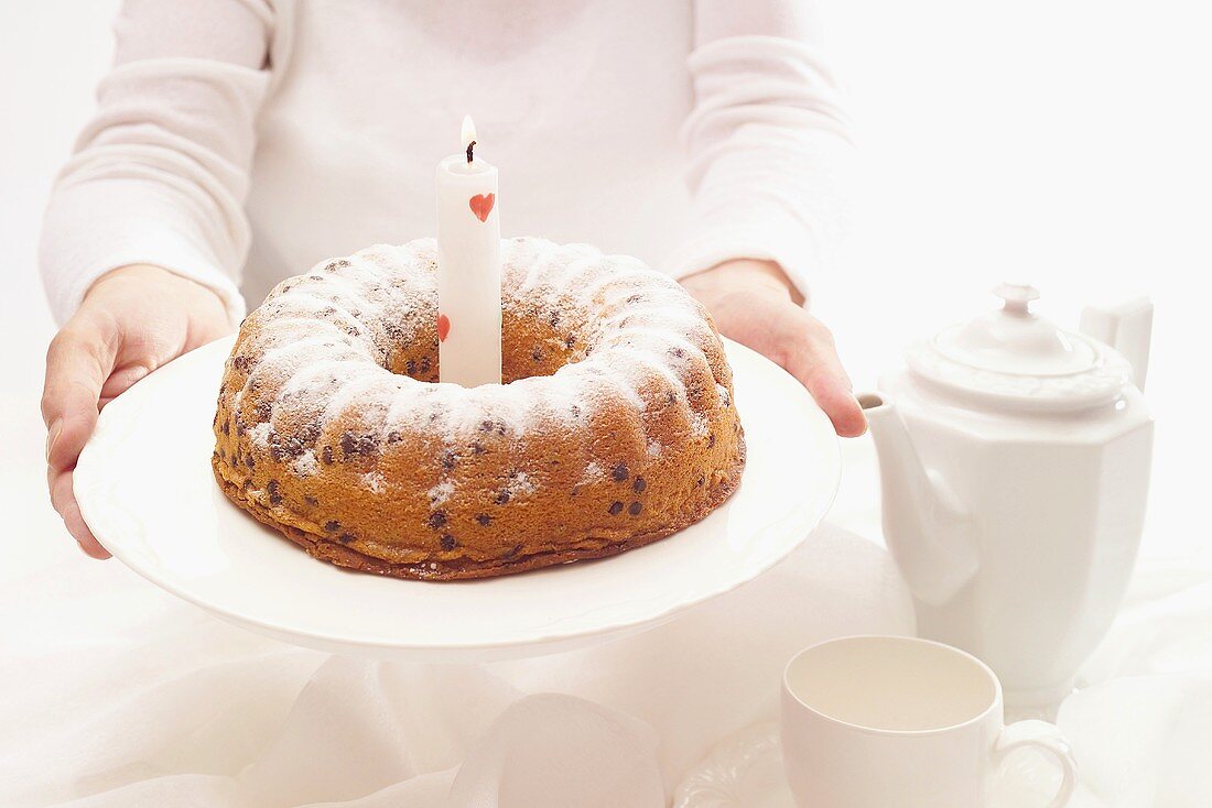 Woman holding out birthday cake with one candle